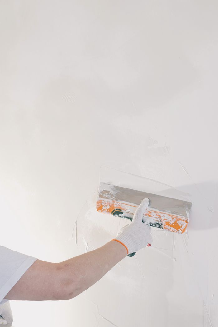 Crop anonymous male in gloves holding spatula and plastering walls in room at home