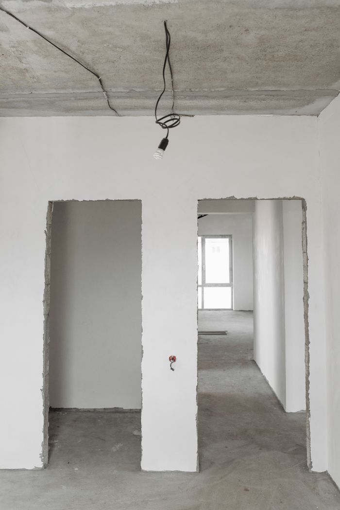 Unfinished room interior with white plastered walls and exposed ceiling in a construction site.